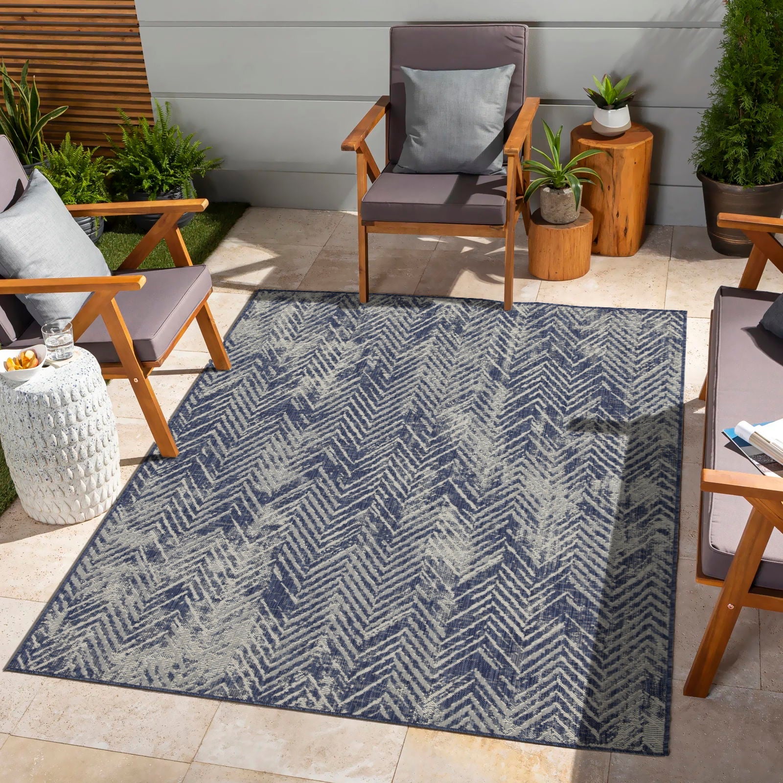 Outdoor patio with a blue patterned rug, wooden chairs, and potted plants.