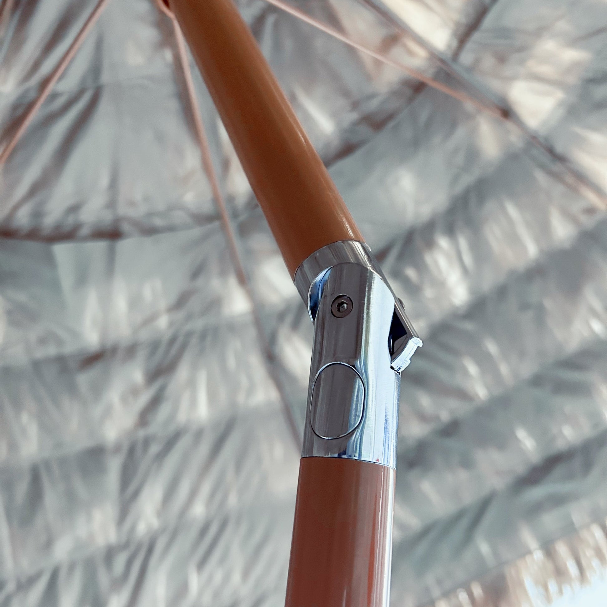 Close-up of a brown umbrella handle with a metallic lock mechanism against a blurred background.