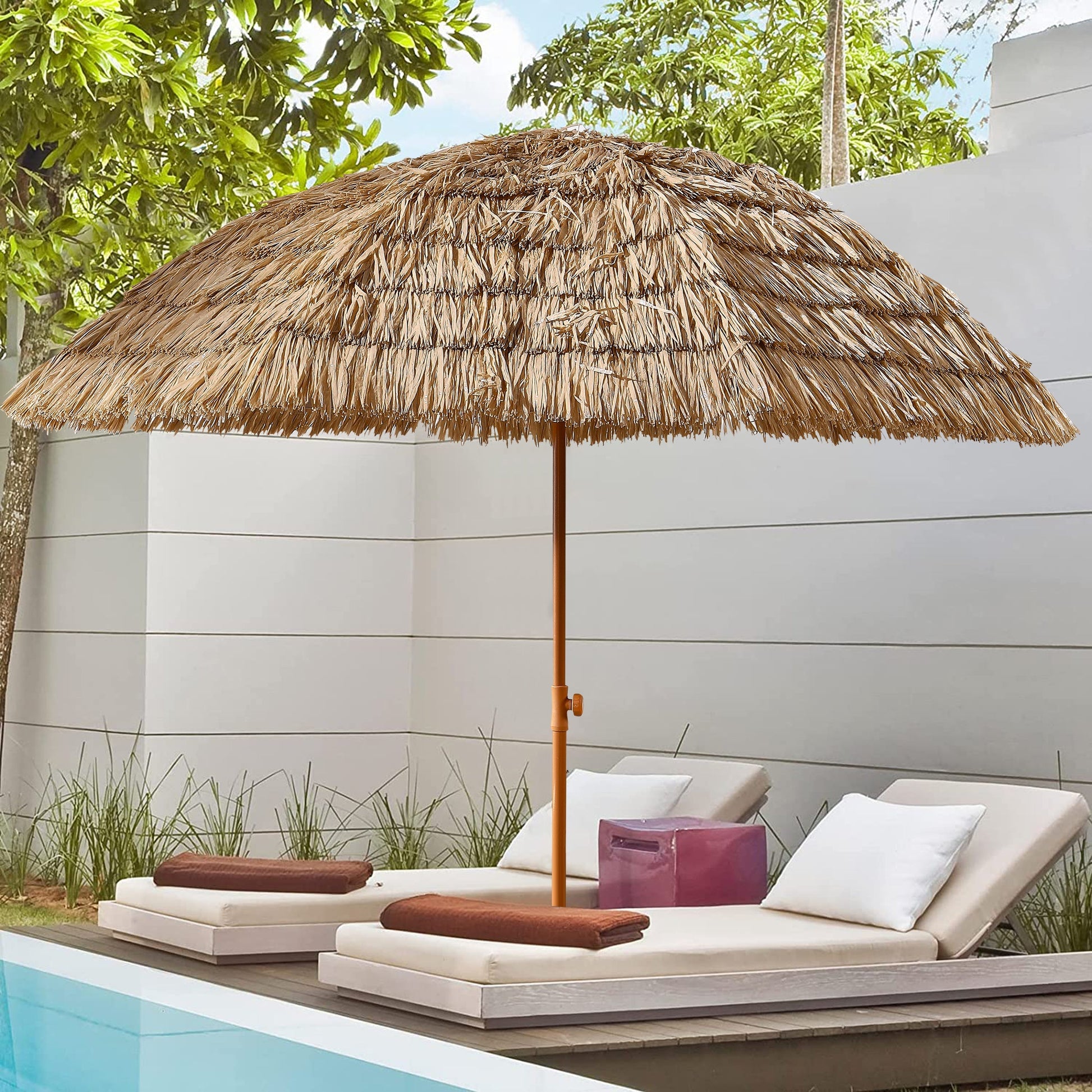 Thatched umbrella over lounge chairs by a poolside with greenery in the background