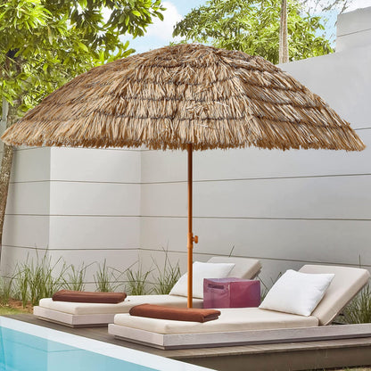 Thatched umbrella over lounge chairs by a poolside with greenery in the background
