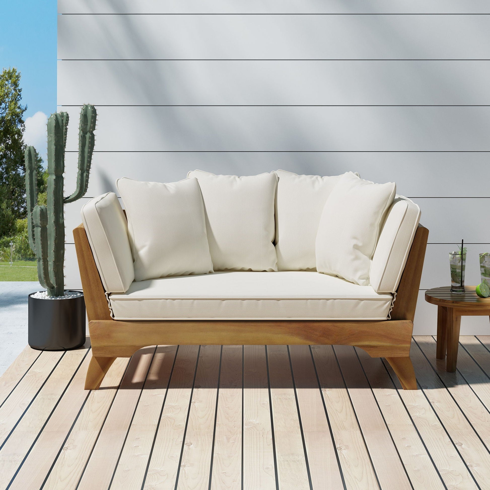 Wooden outdoor sofa with white cushions on a wooden deck, with a cactus plant in the background.