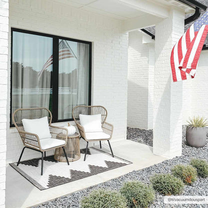 Outdoor patio area with two wicker chairs, a small table, and decorative elements on a white brick house.