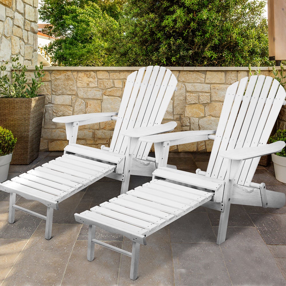 Two white Adirondack chairs on a stone patio with a stone wall and greenery in the background.