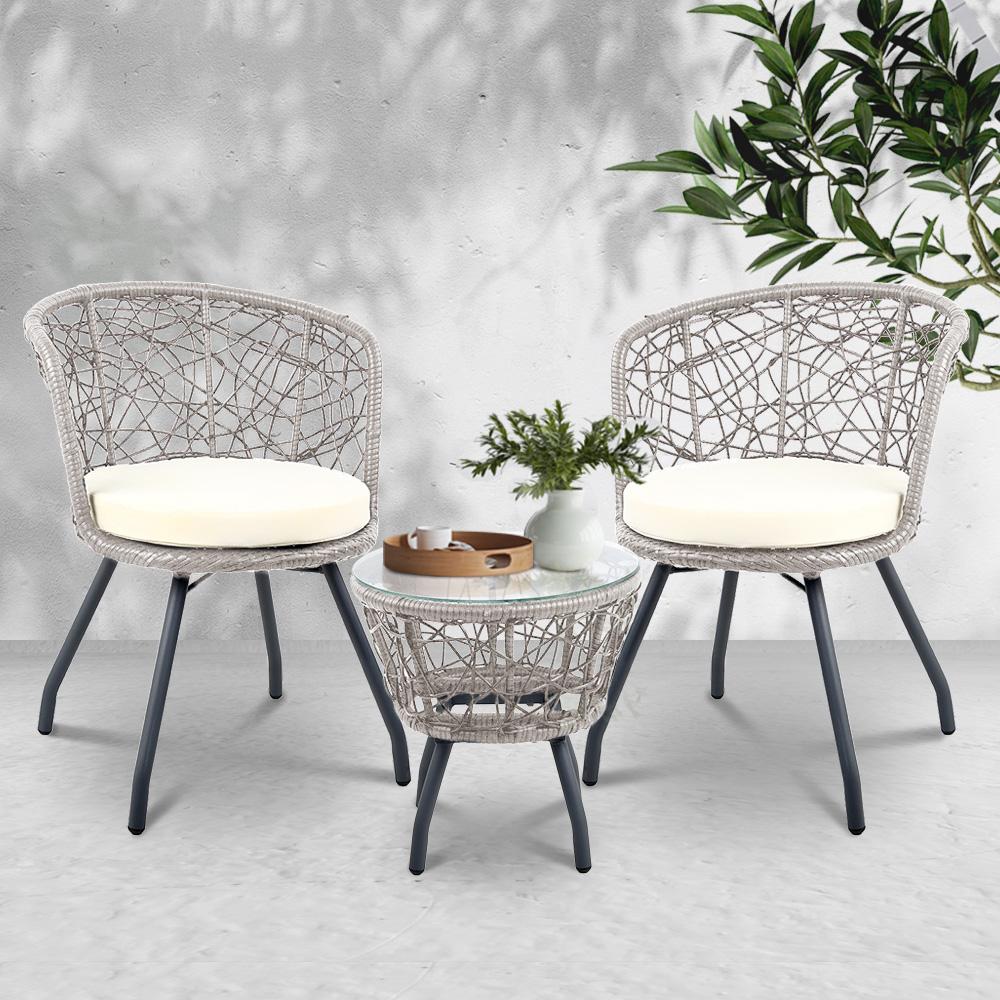Two wicker chairs with white cushions and a matching side table on a light gray floor.
