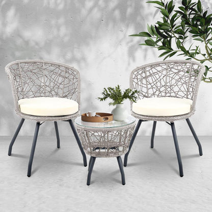 Two wicker chairs with white cushions and a matching side table on a light gray floor.