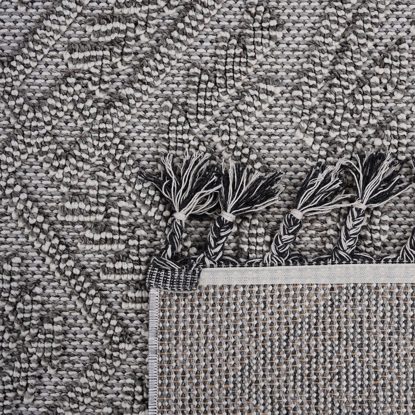Close-up of a textured gray rug with tassels at the corner.