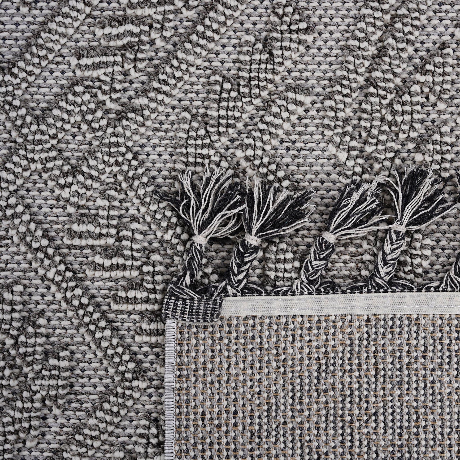Close-up of a textured gray rug with tassels at the corner.