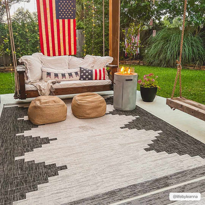 Outdoor patio with a wooden swing, cushions, and a rug on a grassy area.