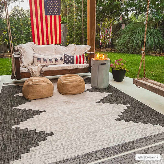 Outdoor patio with a wooden swing, cushions, and a rug on a grassy area.